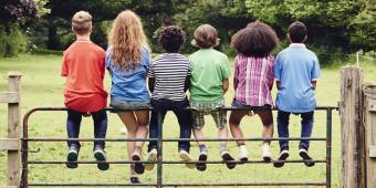 Line of young children sitting on a fence outside with their backs facing the camera